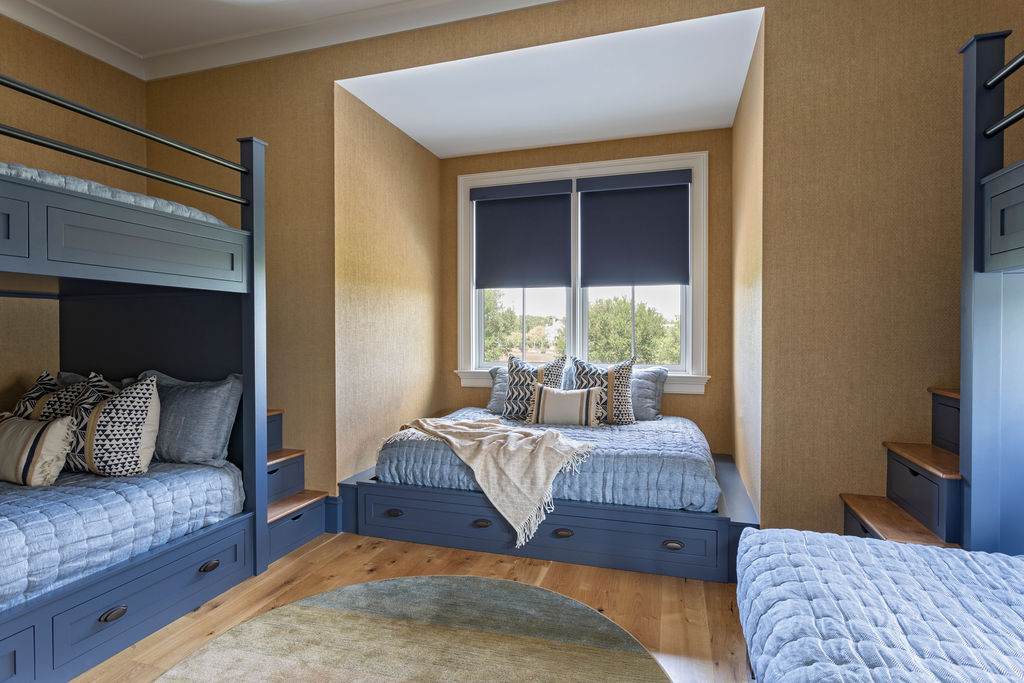 A cozy bunk room with neutral walls, light hardwood floors, and dark blue painted bunk beds with built-in drawers and storage.